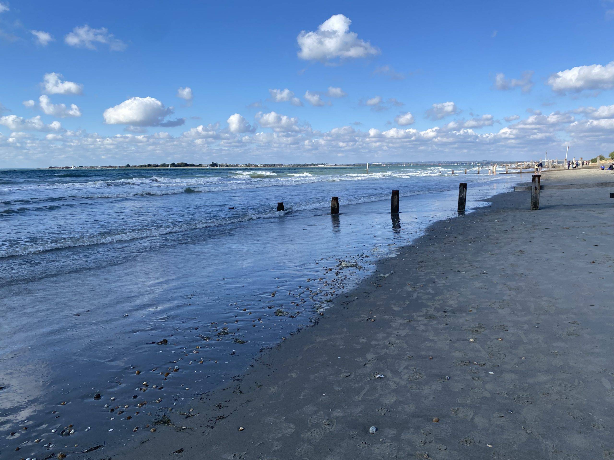 Shoreline with blue sky and clouds and white horses atop the waves in the distance.