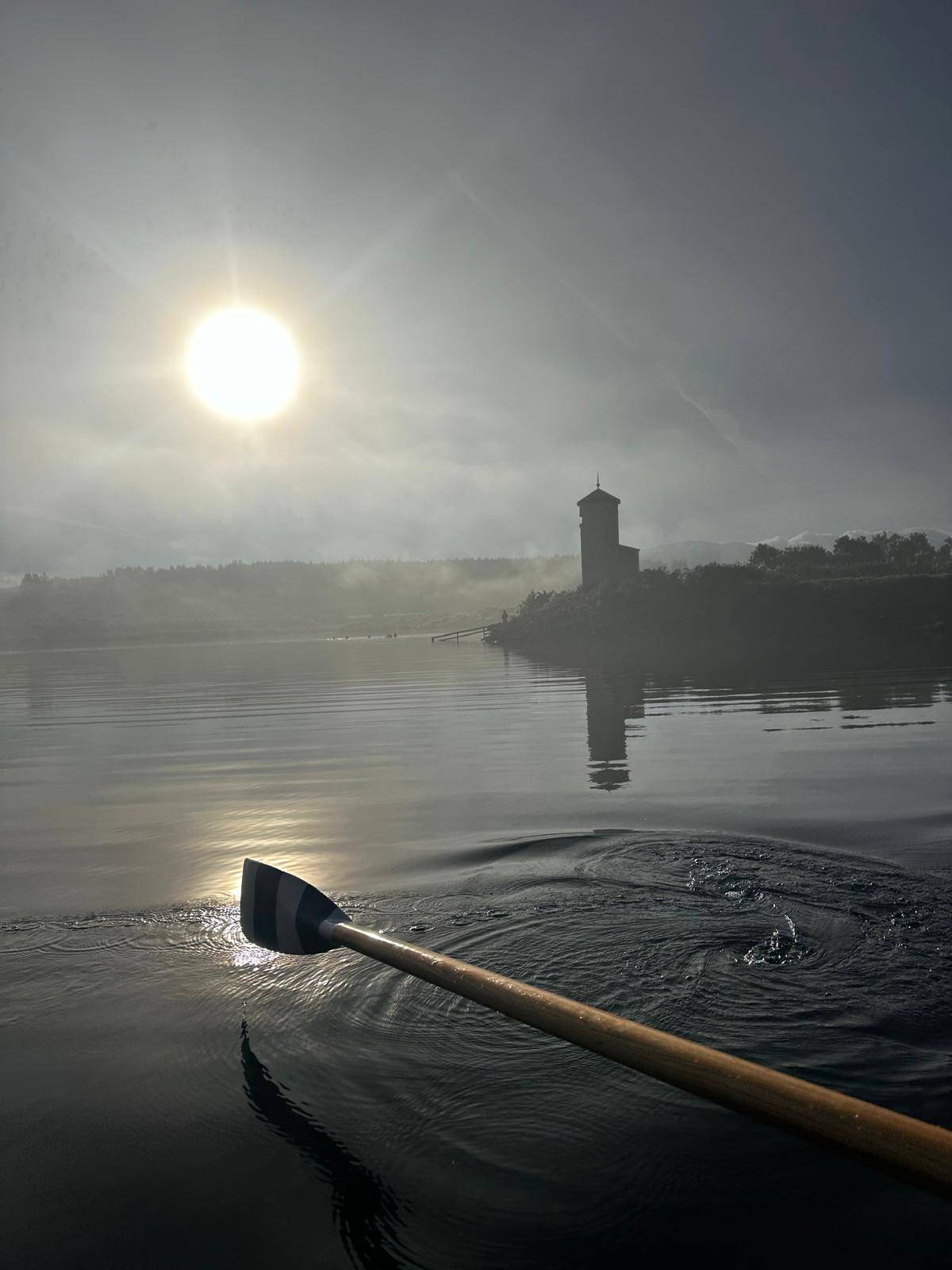 Sunrise over a lake with an oar appearing to glow in the light's reflection on the water. Encouraging over-coming self-doubt through evocative setting.
