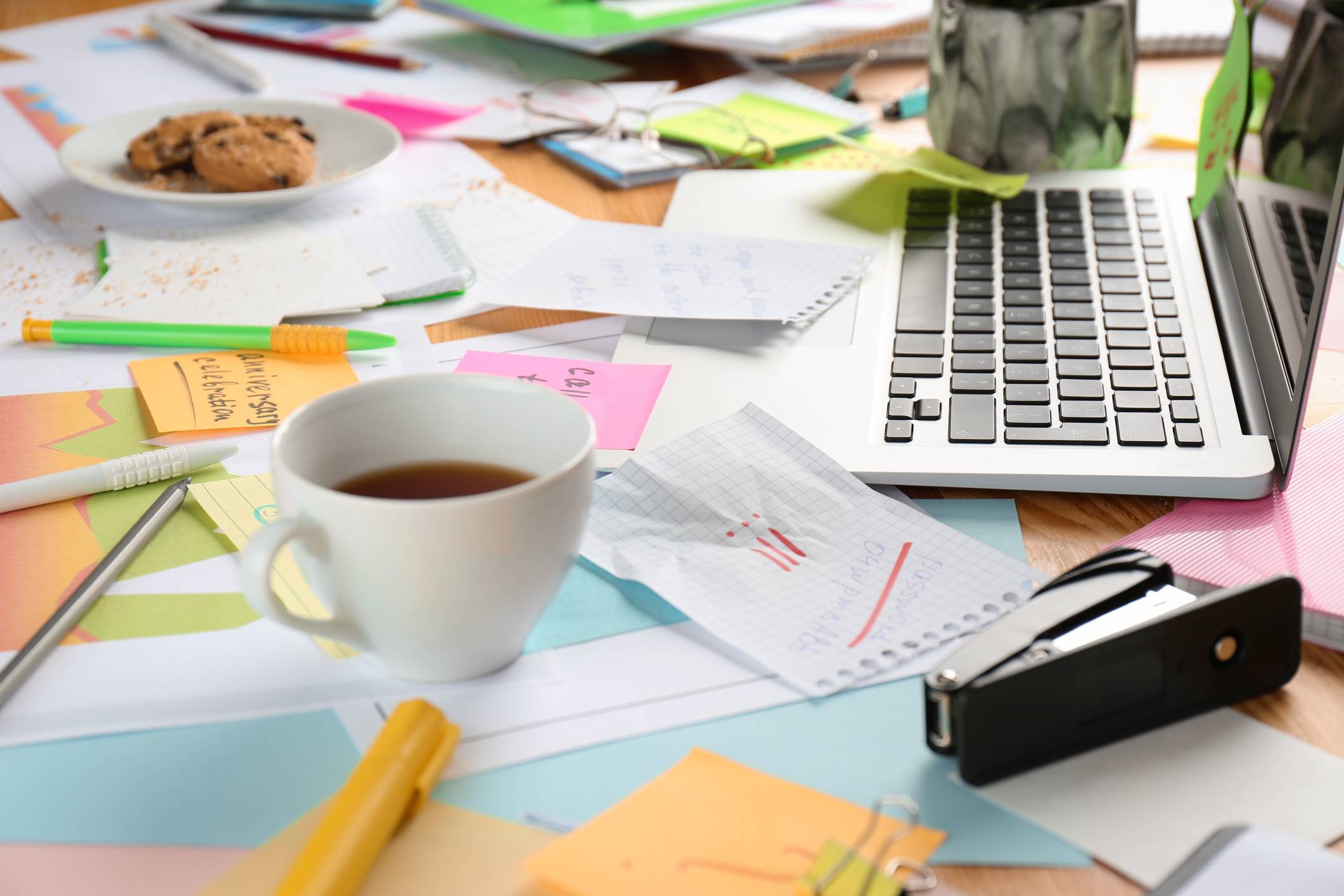 A messy table cluttered with papers and notes. Concept of being overwhelmed by work.