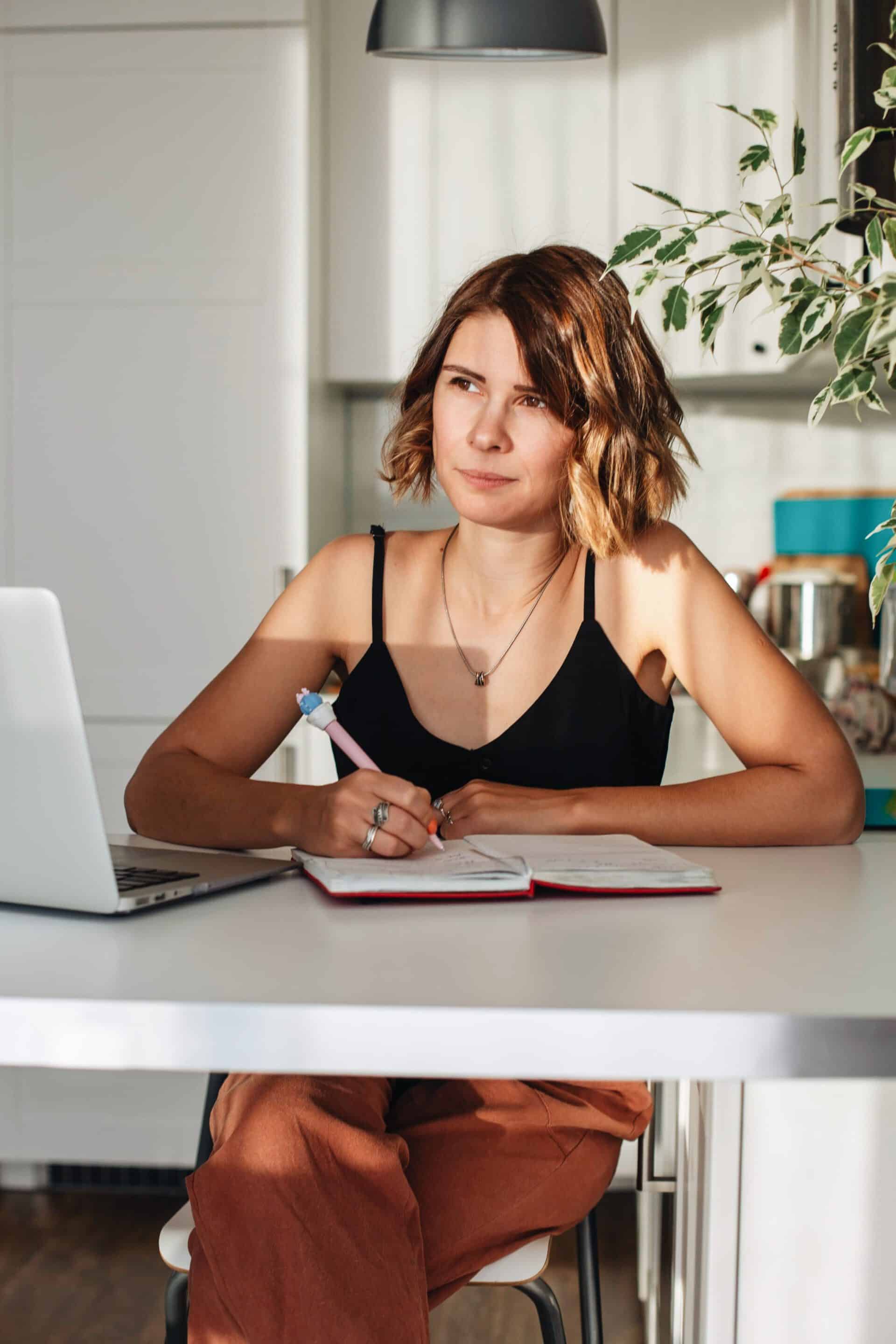 Woman sitting at a desk making notes and thinking.